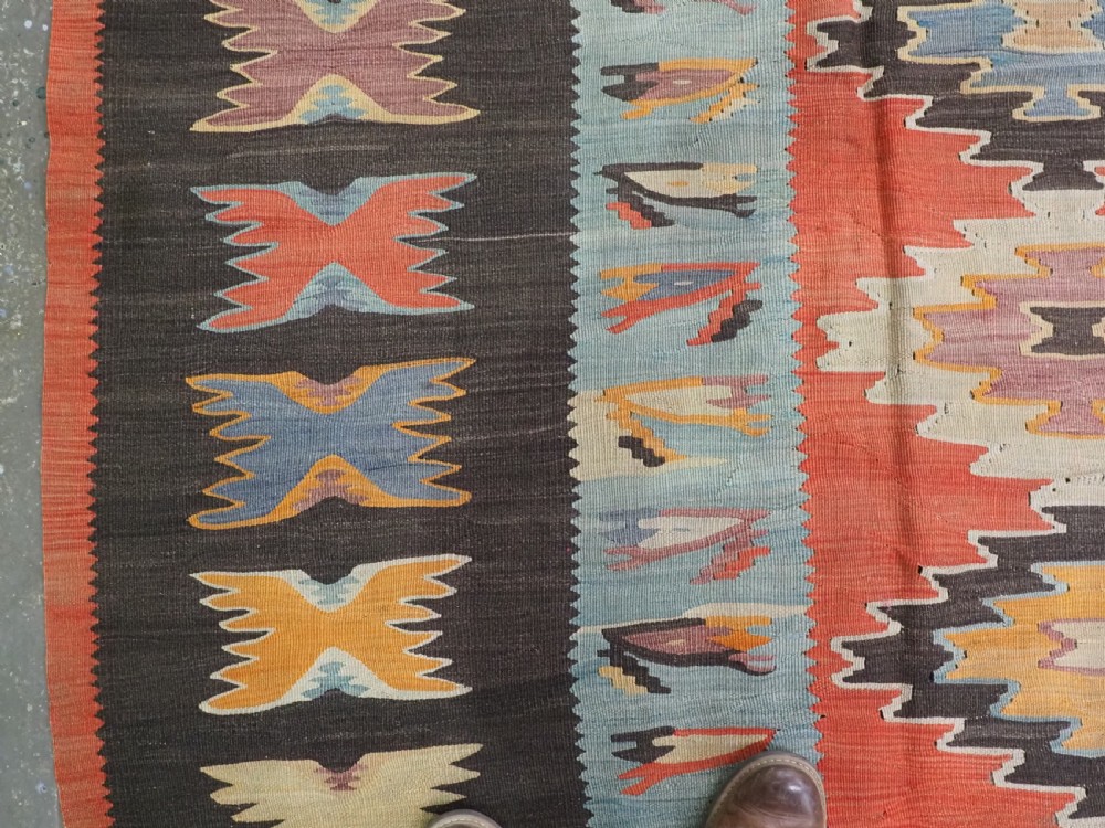 A large antique Pirot Sarkoy flat-weave wool kilim carpet featuring repeating diamond medallions on a terracotta field with dark geometric borders. View VI