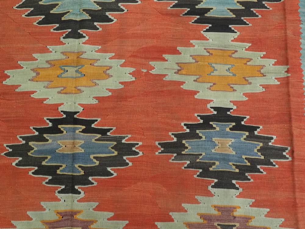 A large antique Pirot Sarkoy flat-weave wool kilim carpet featuring repeating diamond medallions on a terracotta field with dark geometric borders. View IX