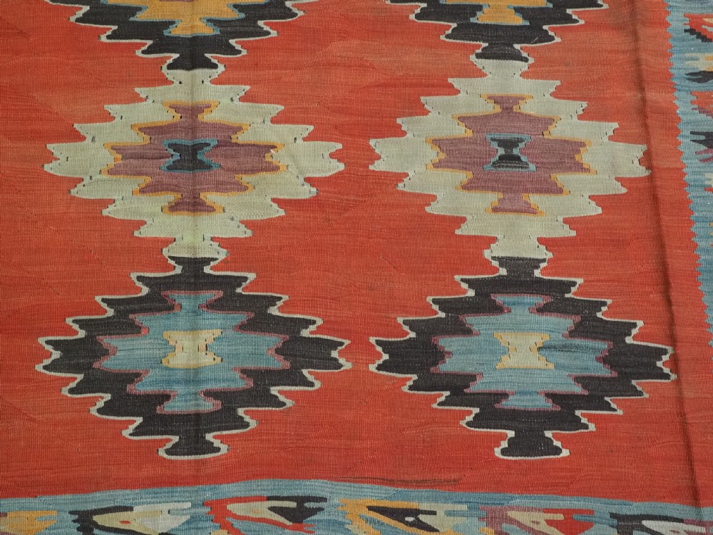 A large antique Pirot Sarkoy flat-weave wool kilim carpet featuring repeating diamond medallions on a terracotta field with dark geometric borders. View X