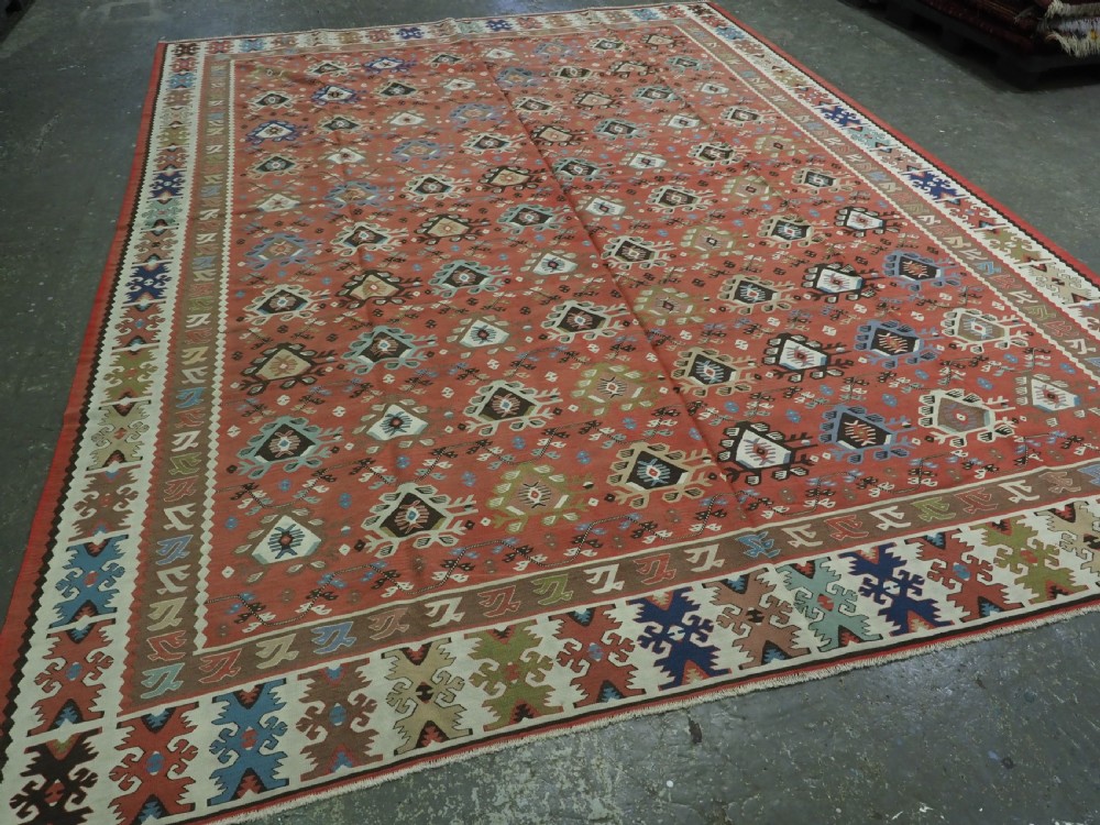 An antique handwoven wool kilim rug featuring a terracotta central field with geometric repeat motifs and patterned borders. View II