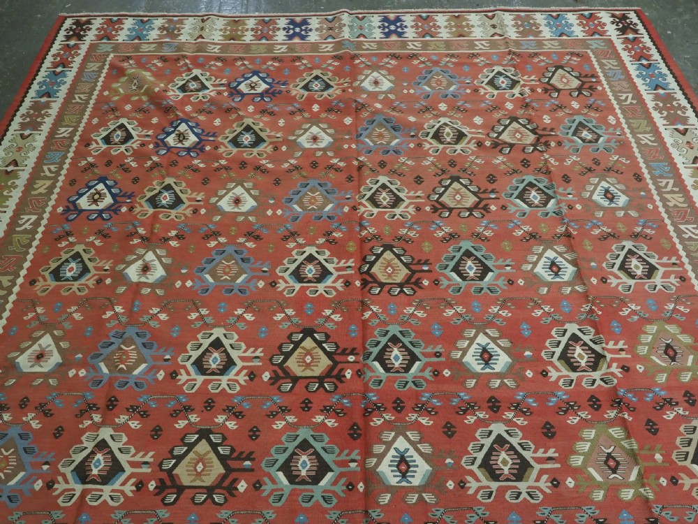 An antique handwoven wool kilim rug featuring a terracotta central field with geometric repeat motifs and patterned borders. View III