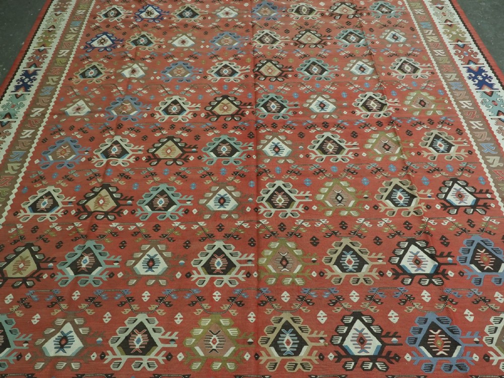 An antique handwoven wool kilim rug featuring a terracotta central field with geometric repeat motifs and patterned borders. View IV