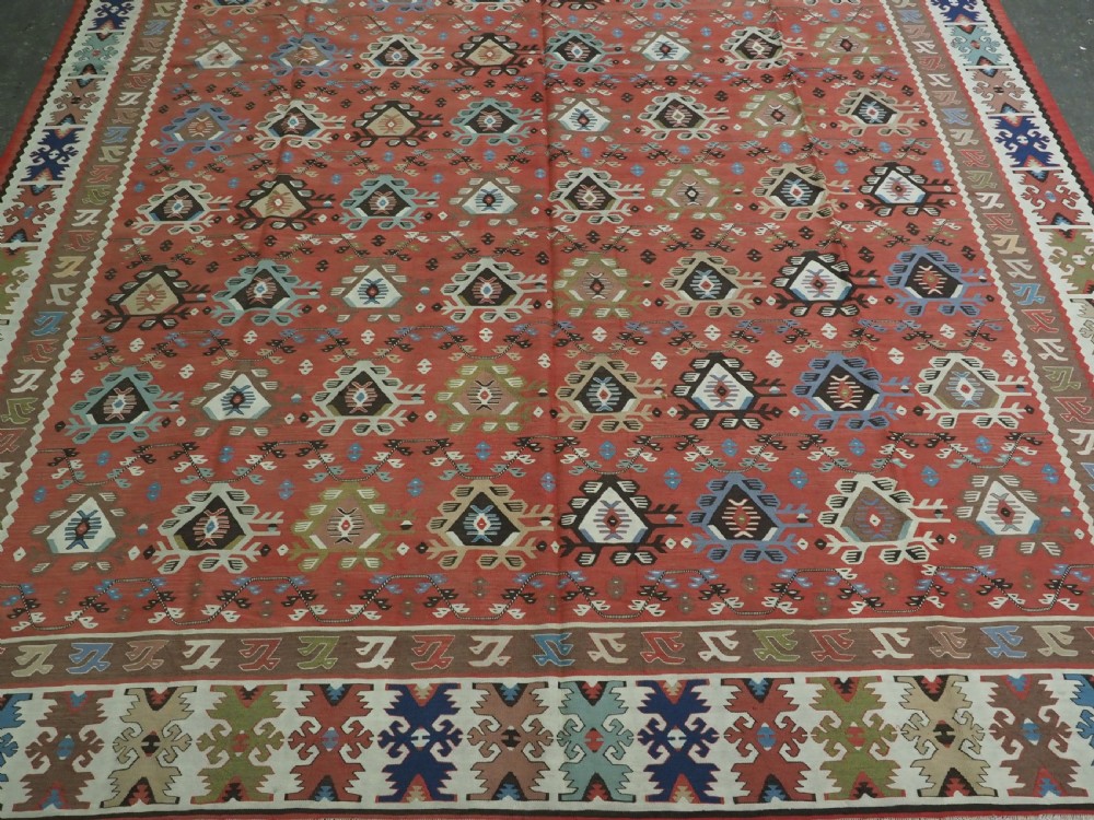 An antique handwoven wool kilim rug featuring a terracotta central field with geometric repeat motifs and patterned borders. View V
