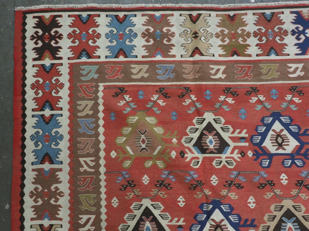 An antique handwoven wool kilim rug featuring a terracotta central field with geometric repeat motifs and patterned borders. View VI