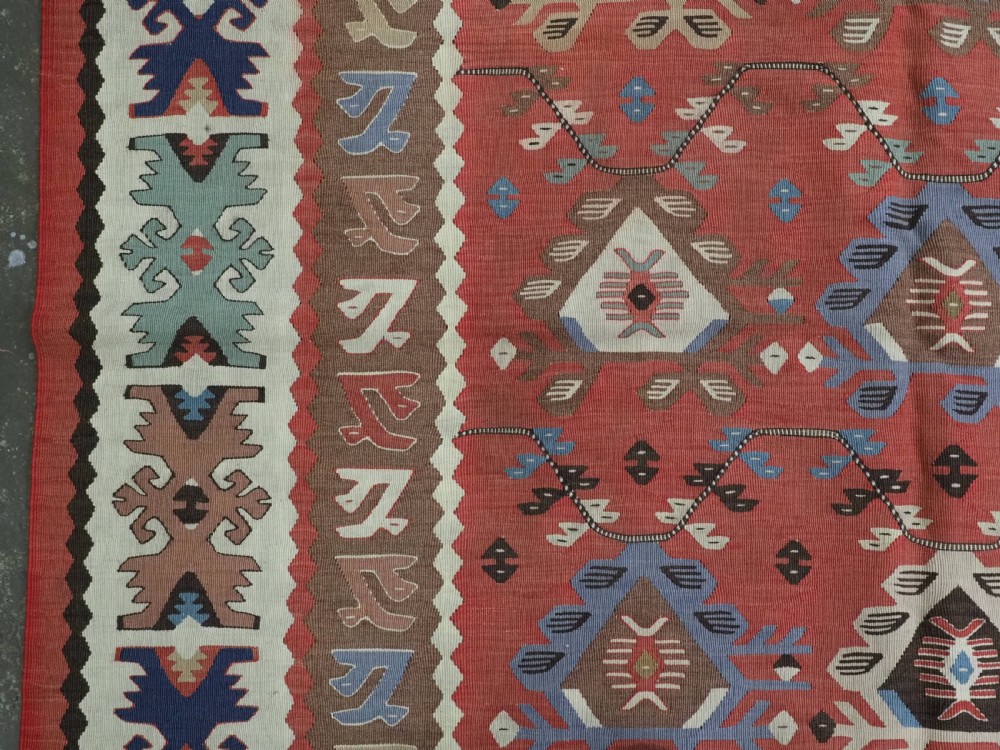 An antique handwoven wool kilim rug featuring a terracotta central field with geometric repeat motifs and patterned borders. View VII