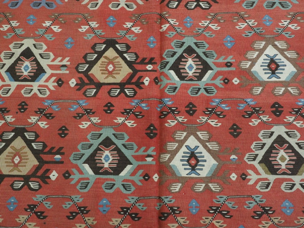 An antique handwoven wool kilim rug featuring a terracotta central field with geometric repeat motifs and patterned borders. View IX