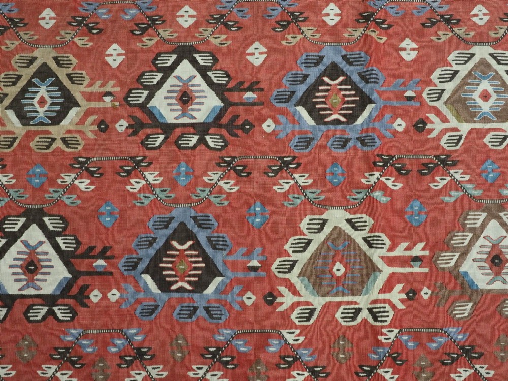 An antique handwoven wool kilim rug featuring a terracotta central field with geometric repeat motifs and patterned borders. View X