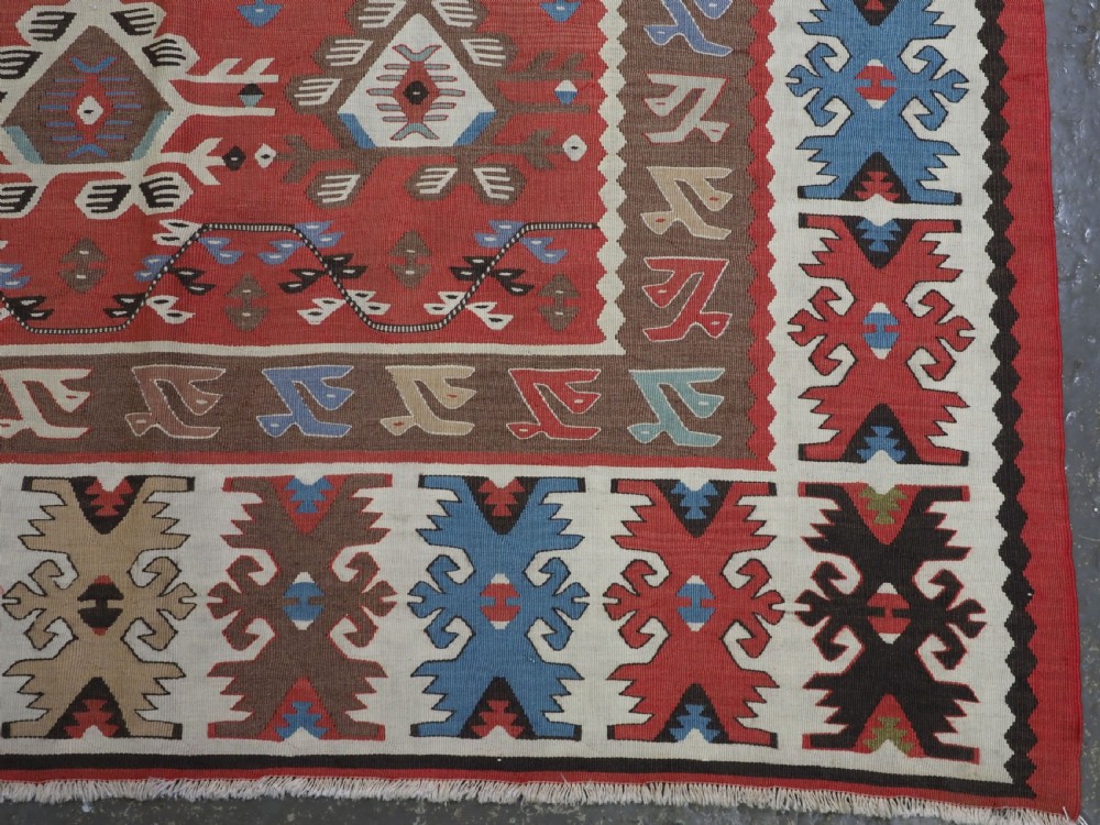 An antique handwoven wool kilim rug featuring a terracotta central field with geometric repeat motifs and patterned borders. View XI