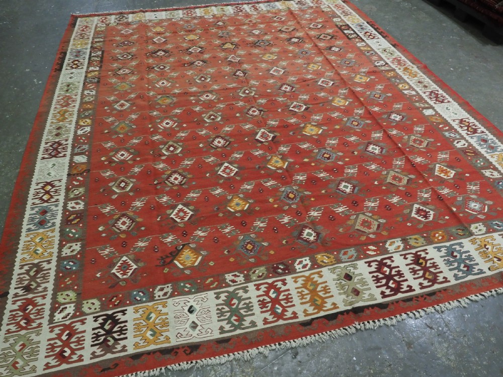 A large antique Pirot Sarkoy flatweave wool kilim rug featuring repeating geometric diamond motifs on a terracotta red field with decorative patterned borders. View II