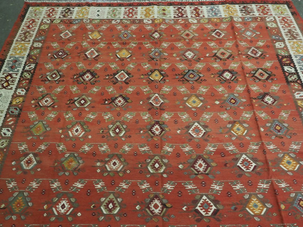 A large antique Pirot Sarkoy flatweave wool kilim rug featuring repeating geometric diamond motifs on a terracotta red field with decorative patterned borders. View III