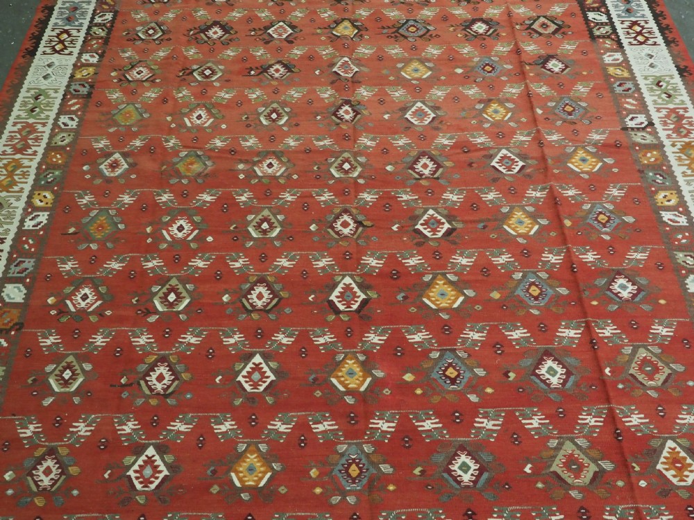A large antique Pirot Sarkoy flatweave wool kilim rug featuring repeating geometric diamond motifs on a terracotta red field with decorative patterned borders. View IV