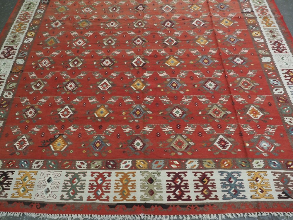 A large antique Pirot Sarkoy flatweave wool kilim rug featuring repeating geometric diamond motifs on a terracotta red field with decorative patterned borders. View V