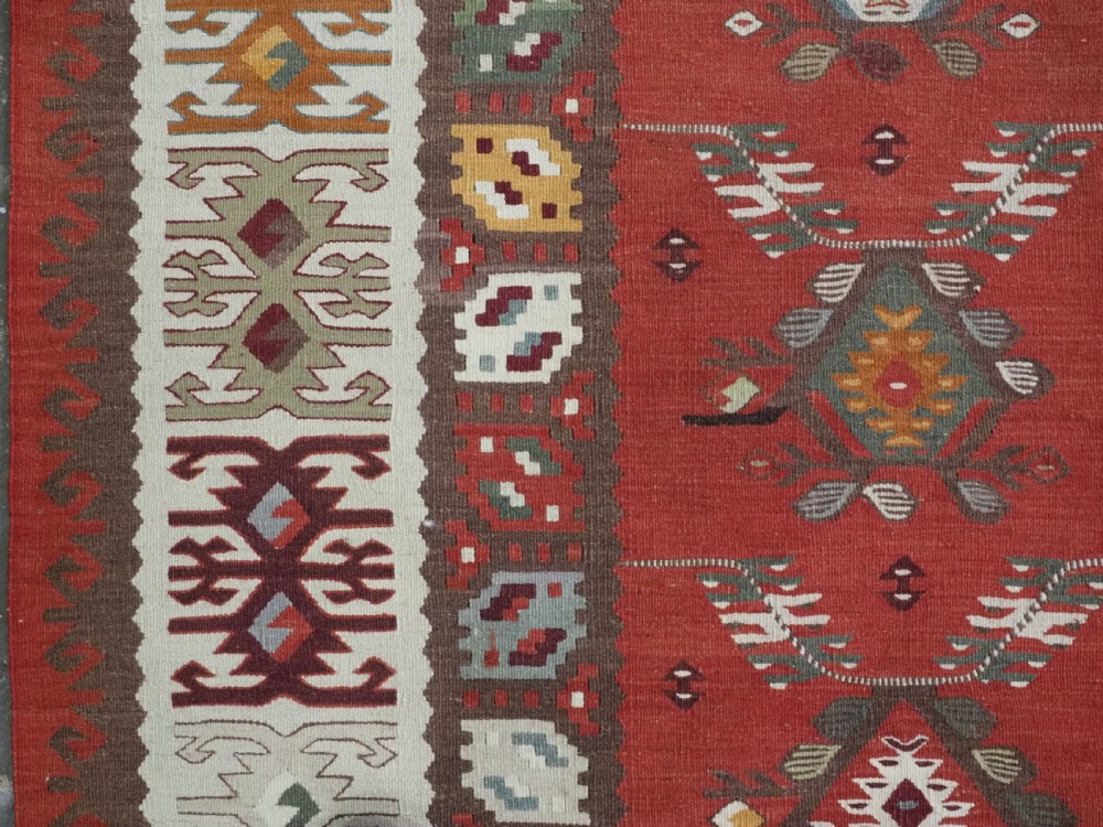 A large antique Pirot Sarkoy flatweave wool kilim rug featuring repeating geometric diamond motifs on a terracotta red field with decorative patterned borders. View VI