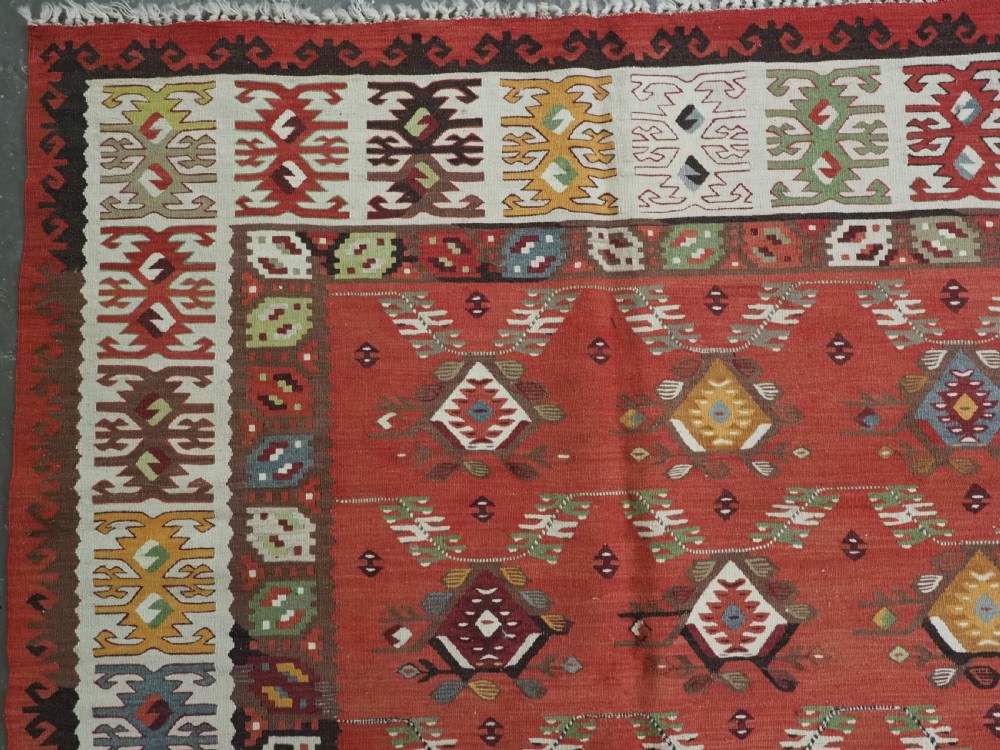 A large antique Pirot Sarkoy flatweave wool kilim rug featuring repeating geometric diamond motifs on a terracotta red field with decorative patterned borders. View VII