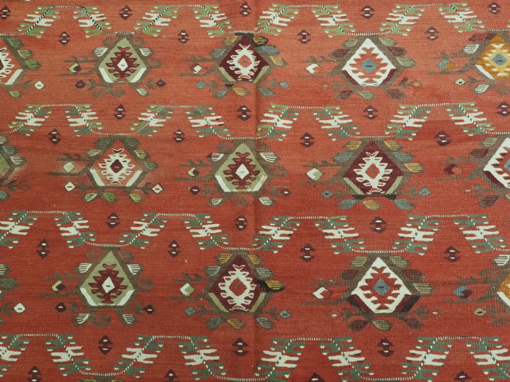 A large antique Pirot Sarkoy flatweave wool kilim rug featuring repeating geometric diamond motifs on a terracotta red field with decorative patterned borders. View IX