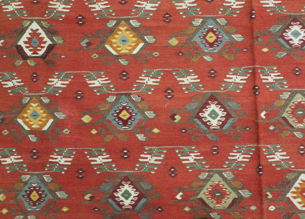 A large antique Pirot Sarkoy flatweave wool kilim rug featuring repeating geometric diamond motifs on a terracotta red field with decorative patterned borders. View X