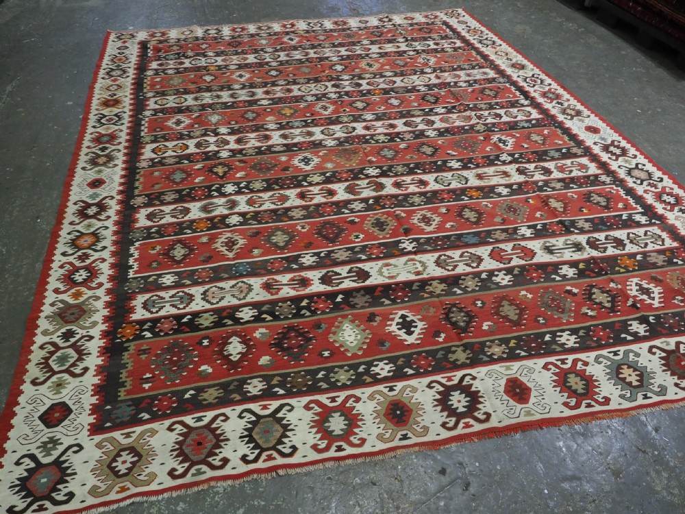 A large handwoven antique kilim rug featuring horizontal bands of intricate geometric motifs in terracotta red, cream, charcoal, and brown hues. View II