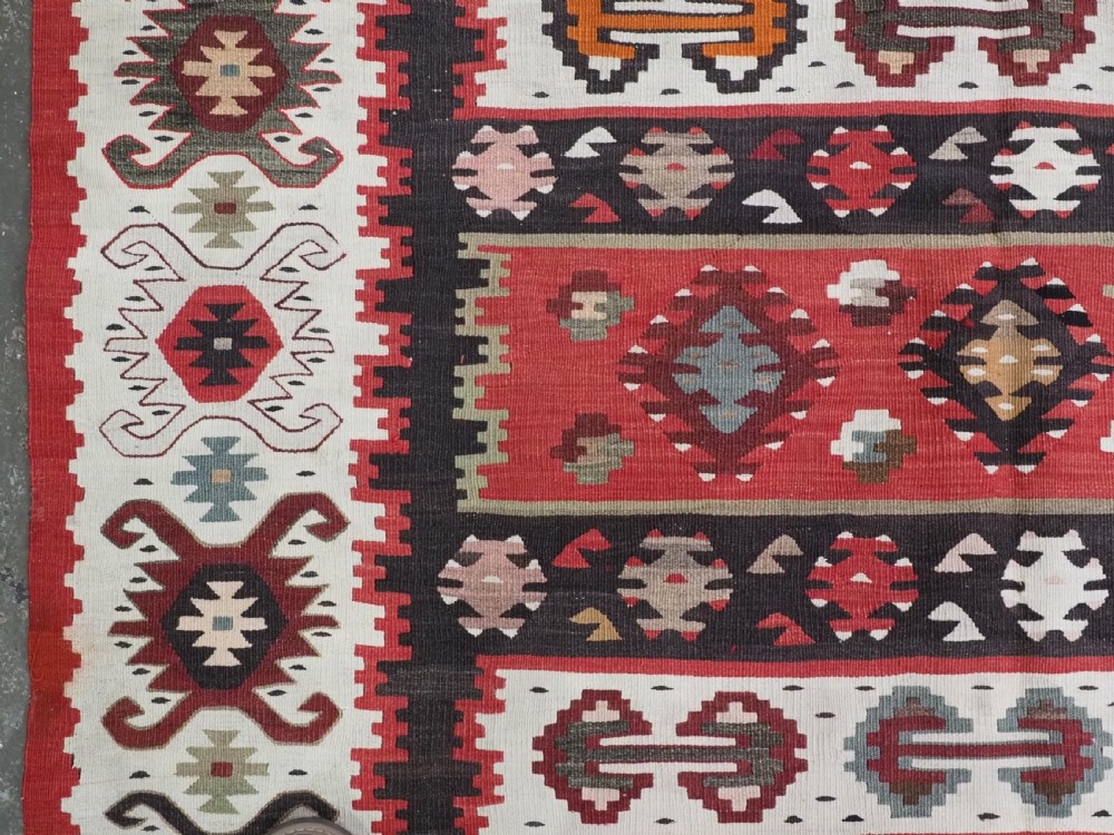 A large handwoven antique kilim rug featuring horizontal bands of intricate geometric motifs in terracotta red, cream, charcoal, and brown hues. View VII