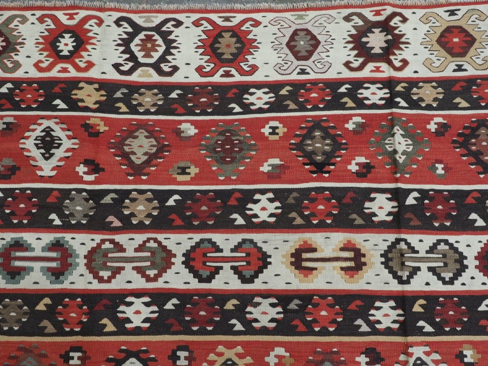 A large handwoven antique kilim rug featuring horizontal bands of intricate geometric motifs in terracotta red, cream, charcoal, and brown hues. View VIII