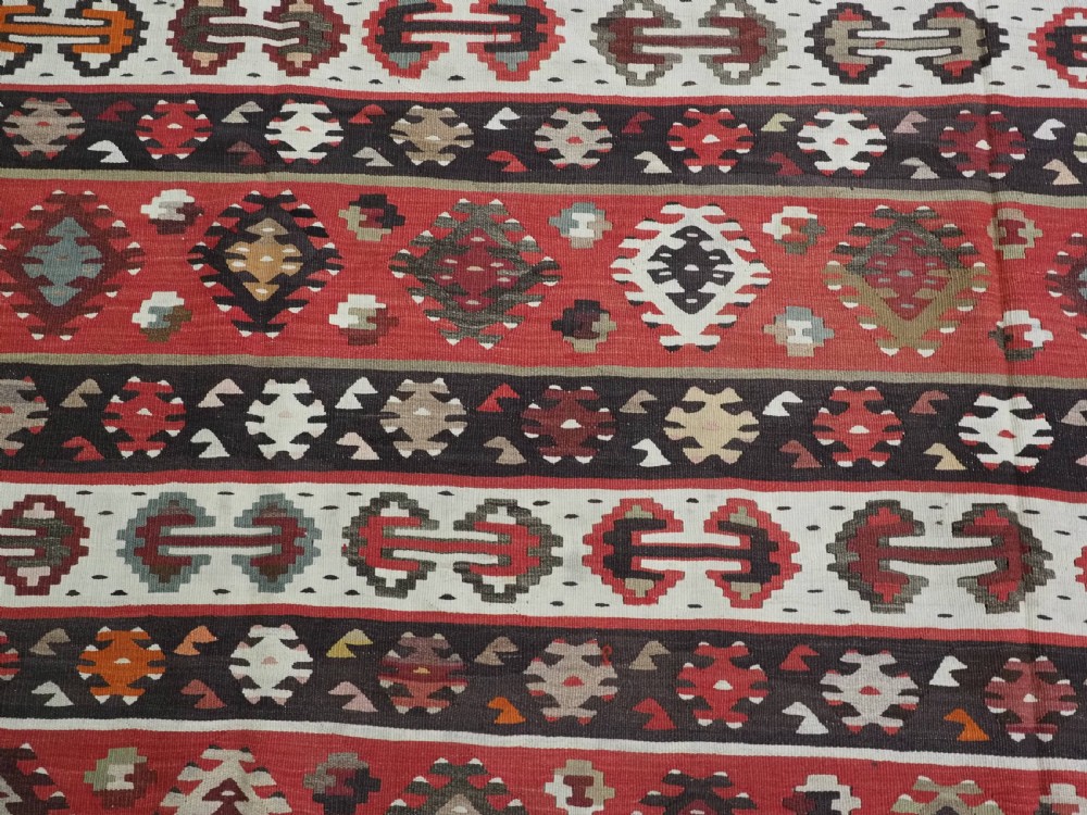 A large handwoven antique kilim rug featuring horizontal bands of intricate geometric motifs in terracotta red, cream, charcoal, and brown hues. View IX