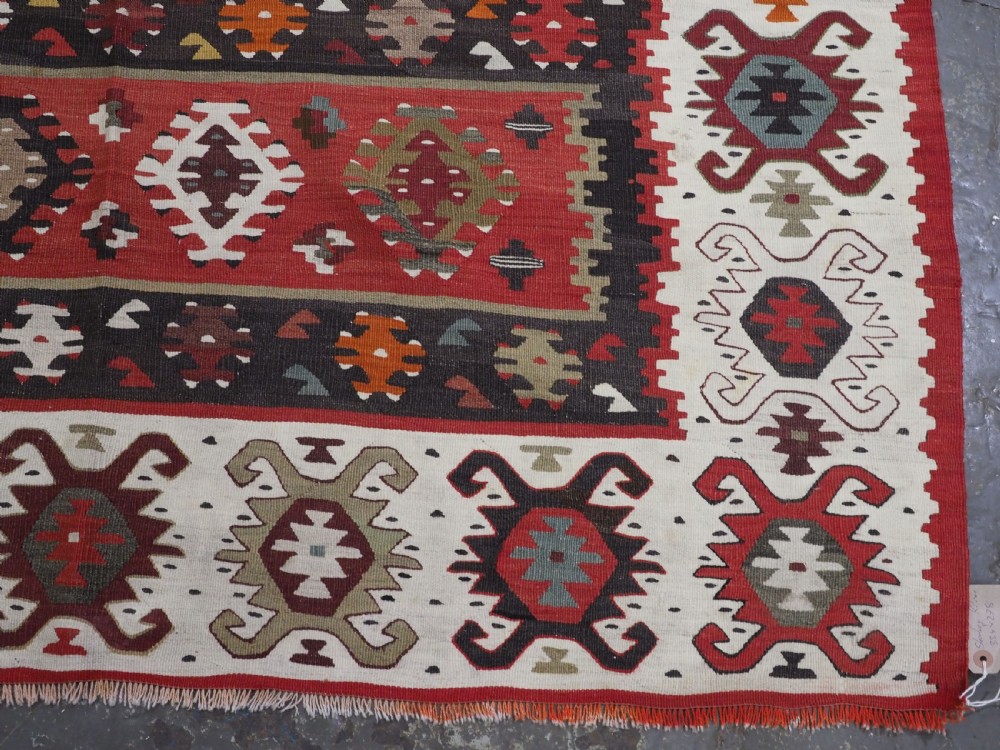 A large handwoven antique kilim rug featuring horizontal bands of intricate geometric motifs in terracotta red, cream, charcoal, and brown hues. View XI