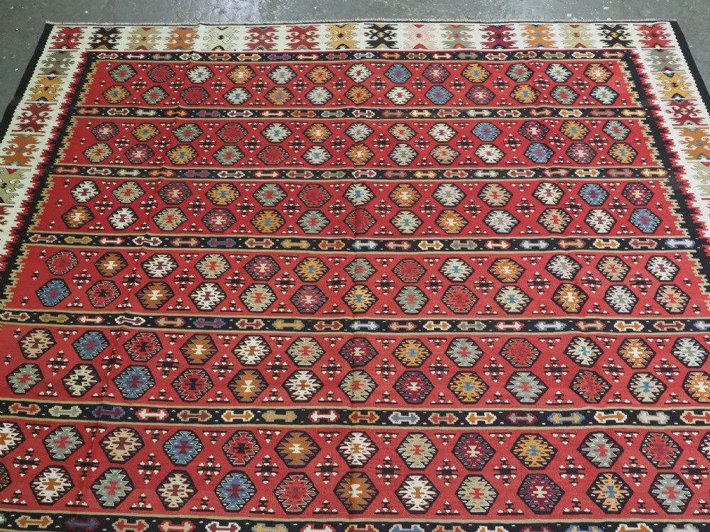 A large antique red flatweave wool kilim rug featuring horizontal bands filled with geometric diamond patterns and detailed multicoloured borders. View III
