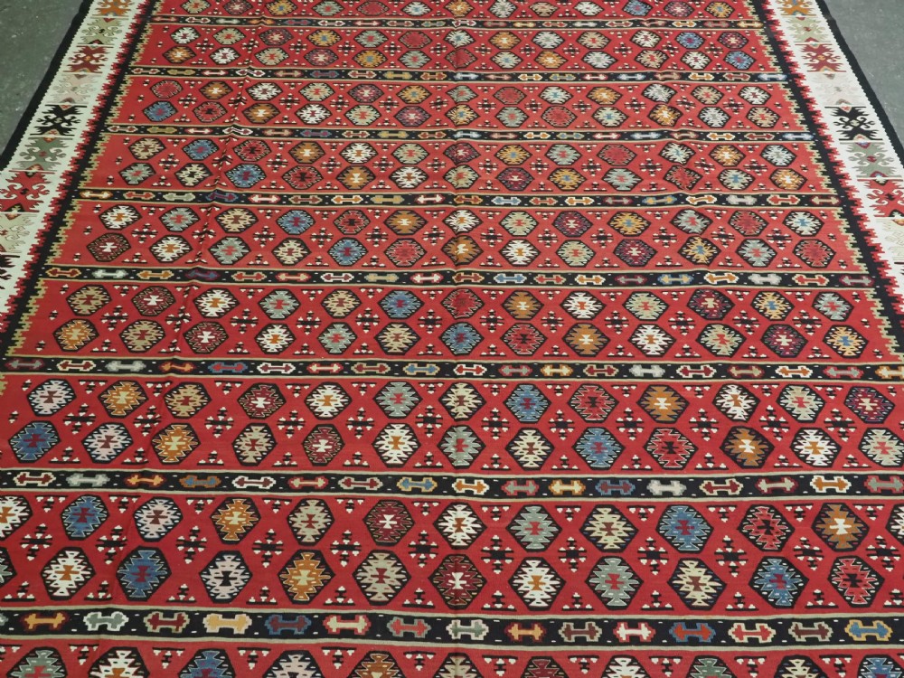 A large antique red flatweave wool kilim rug featuring horizontal bands filled with geometric diamond patterns and detailed multicoloured borders. View IV