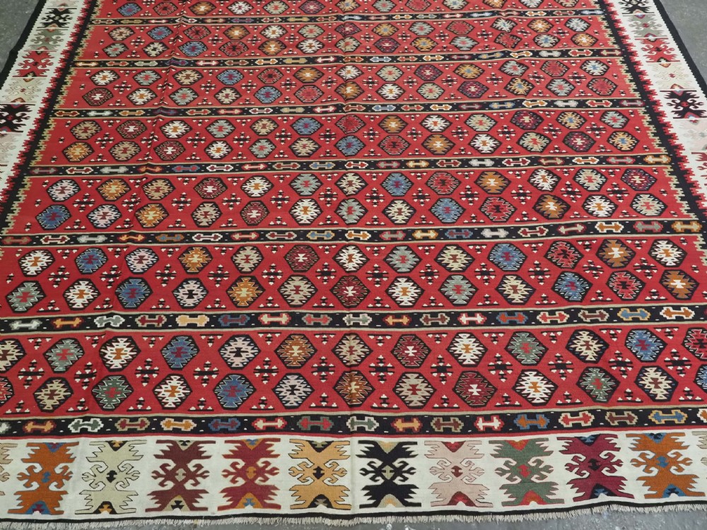 A large antique red flatweave wool kilim rug featuring horizontal bands filled with geometric diamond patterns and detailed multicoloured borders. View V