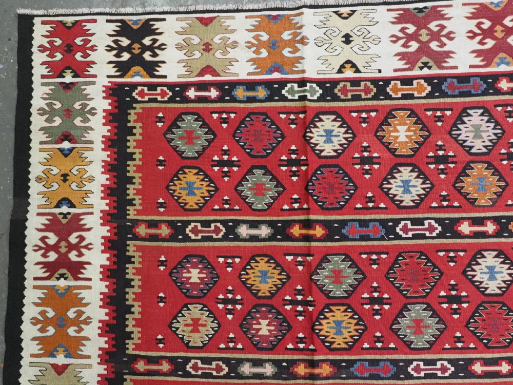 A large antique red flatweave wool kilim rug featuring horizontal bands filled with geometric diamond patterns and detailed multicoloured borders. View VI