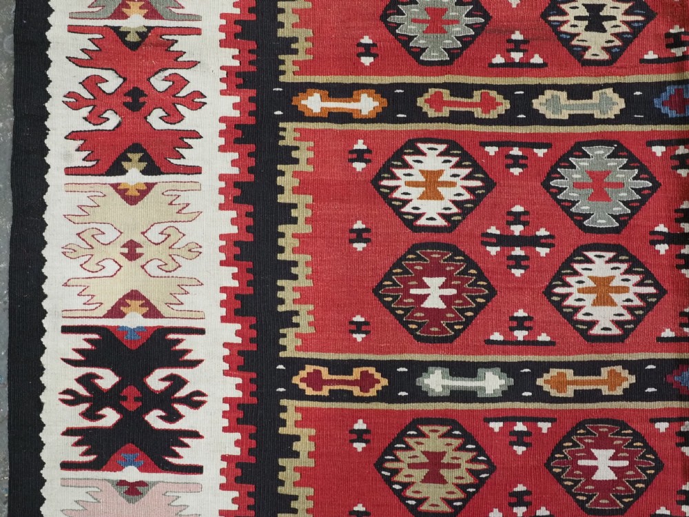 A large antique red flatweave wool kilim rug featuring horizontal bands filled with geometric diamond patterns and detailed multicoloured borders. View VII