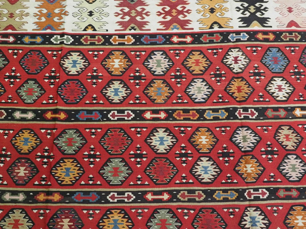 A large antique red flatweave wool kilim rug featuring horizontal bands filled with geometric diamond patterns and detailed multicoloured borders. View VIII