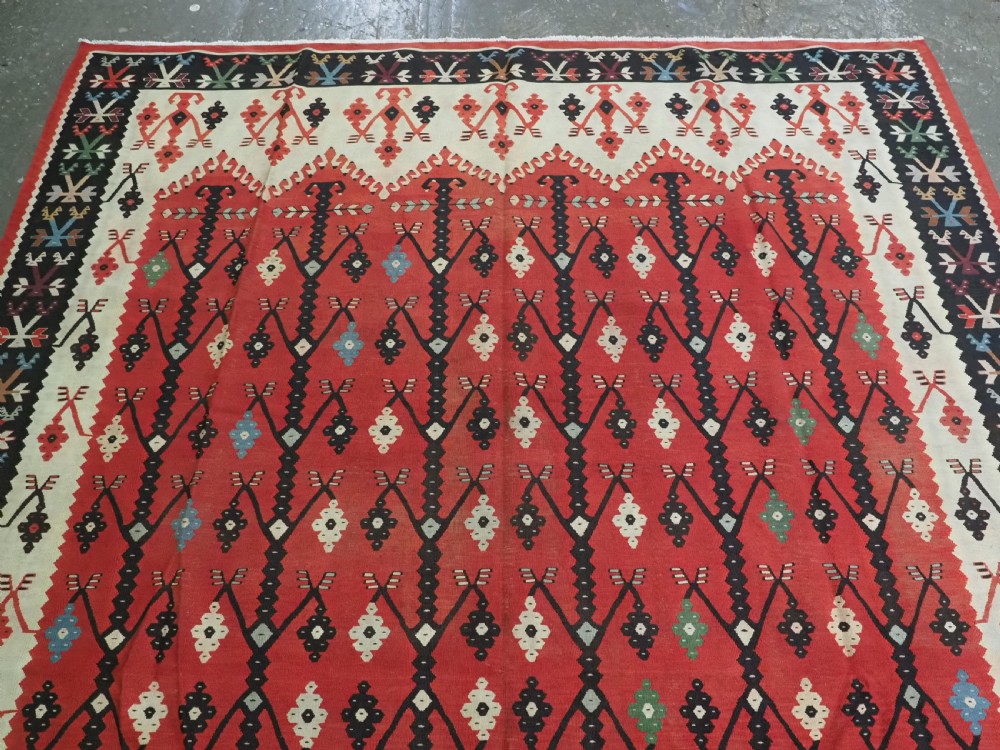 An antique flatweave wool kilim carpet featuring a central red field patterned with vertical flowering tree motifs surrounded by layered geometric borders. View III