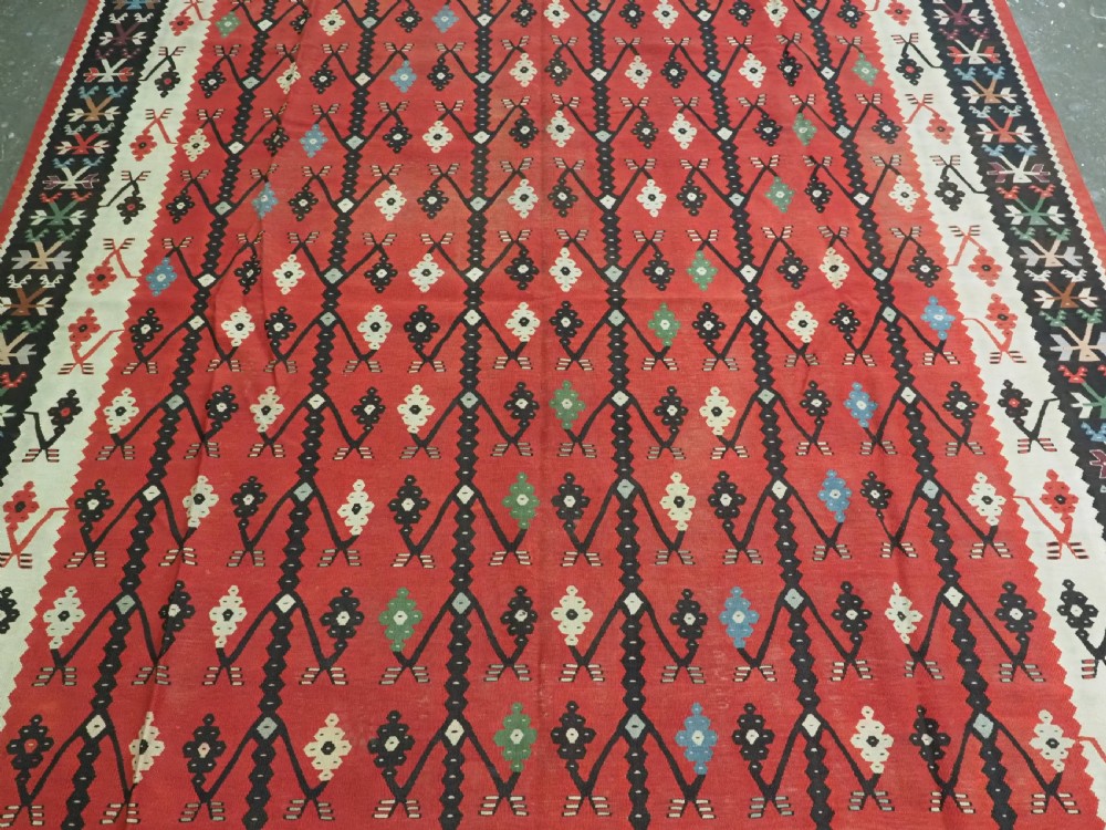 An antique flatweave wool kilim carpet featuring a central red field patterned with vertical flowering tree motifs surrounded by layered geometric borders. View IV
