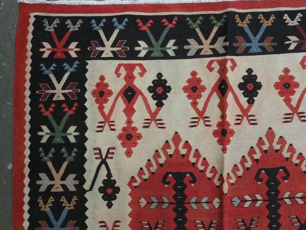 An antique flatweave wool kilim carpet featuring a central red field patterned with vertical flowering tree motifs surrounded by layered geometric borders. View VI