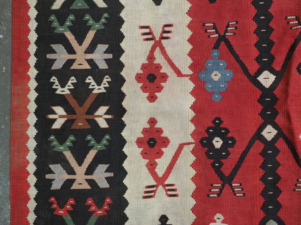 An antique flatweave wool kilim carpet featuring a central red field patterned with vertical flowering tree motifs surrounded by layered geometric borders. View VII