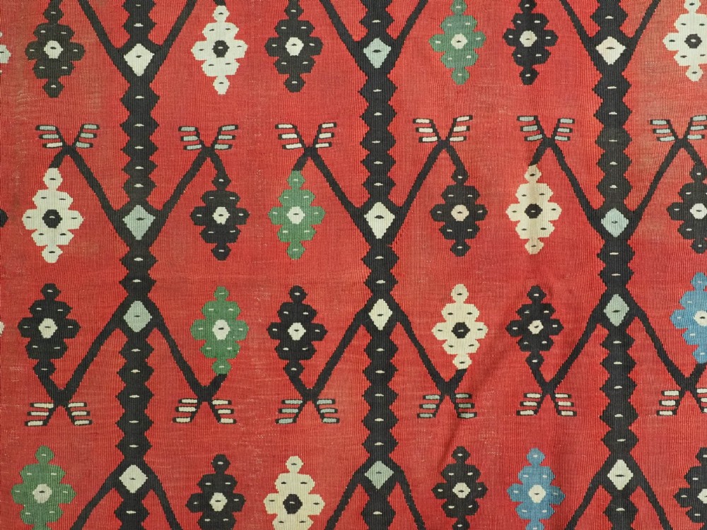An antique flatweave wool kilim carpet featuring a central red field patterned with vertical flowering tree motifs surrounded by layered geometric borders. View IX