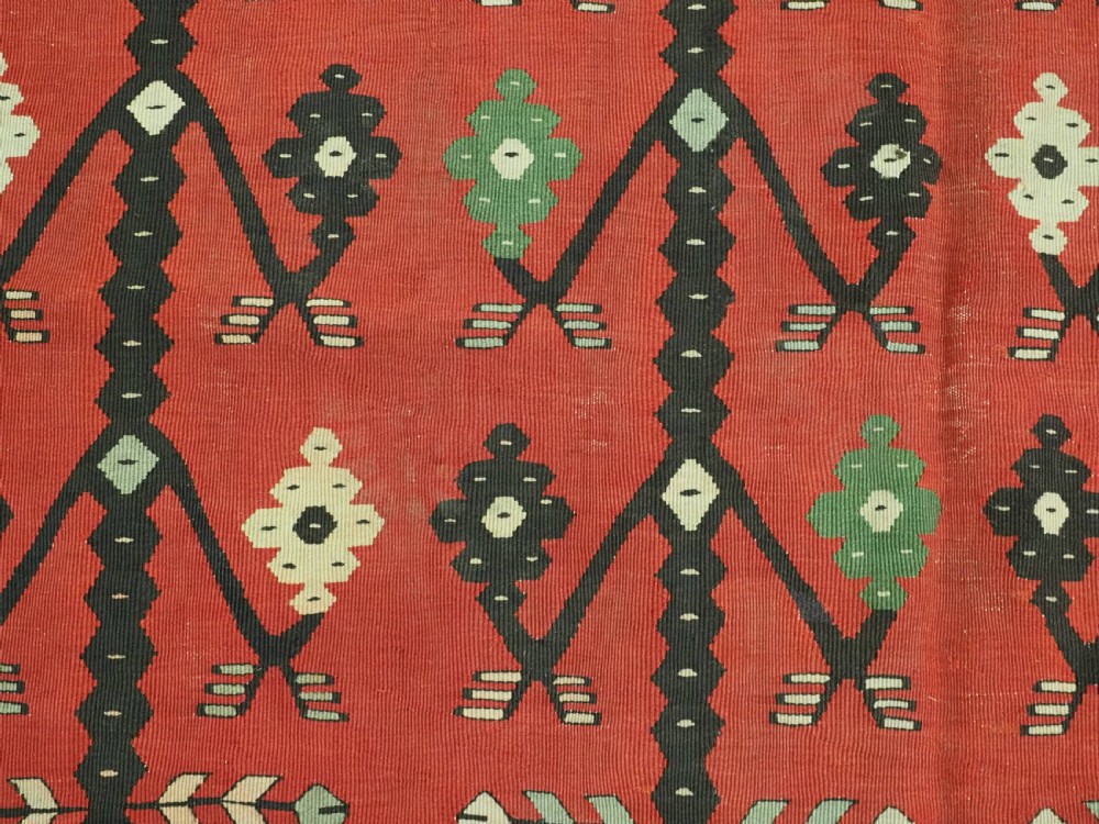 An antique flatweave wool kilim carpet featuring a central red field patterned with vertical flowering tree motifs surrounded by layered geometric borders. View X