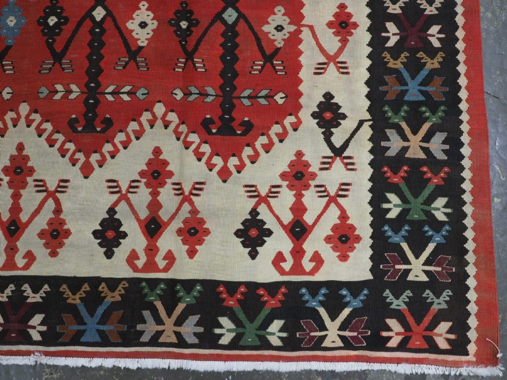 An antique flatweave wool kilim carpet featuring a central red field patterned with vertical flowering tree motifs surrounded by layered geometric borders. View XI