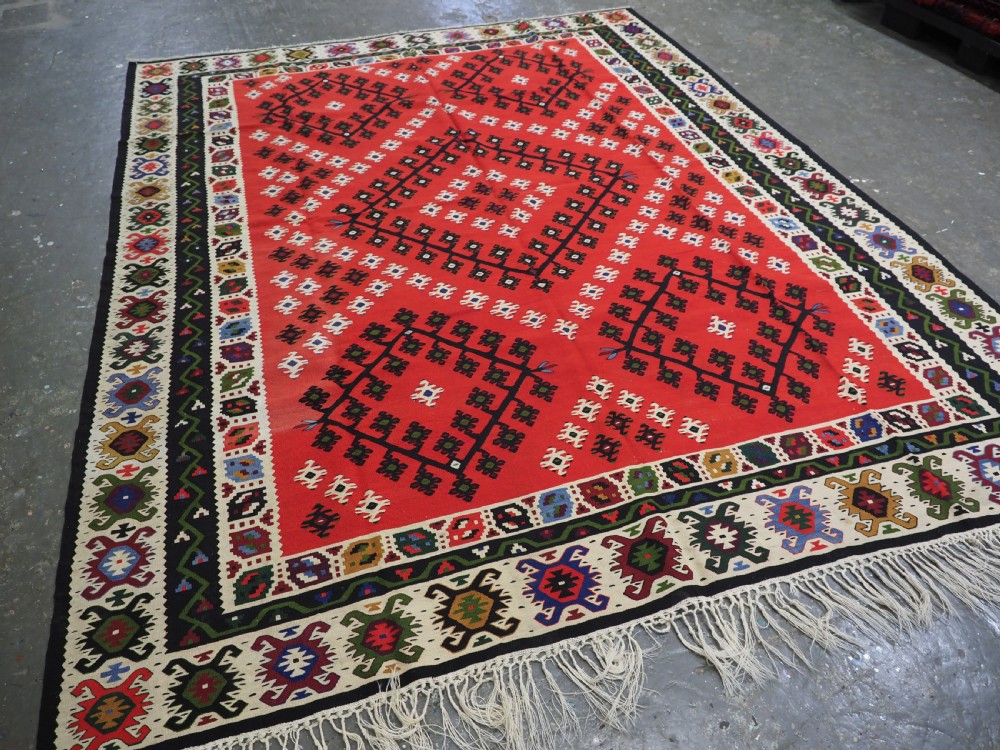 An antique red Pirot Sarkoy wool kilim rug featuring black and white geometric diamond motifs and multi-coloured decorative borders. View II