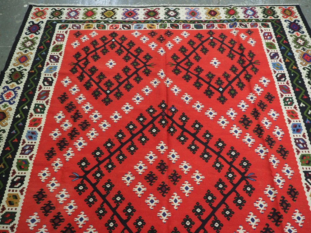 An antique red Pirot Sarkoy wool kilim rug featuring black and white geometric diamond motifs and multi-coloured decorative borders. View III