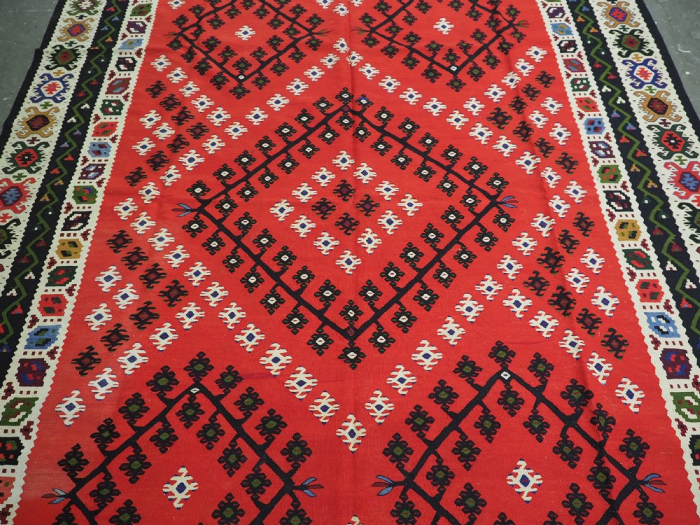 An antique red Pirot Sarkoy wool kilim rug featuring black and white geometric diamond motifs and multi-coloured decorative borders. View IV