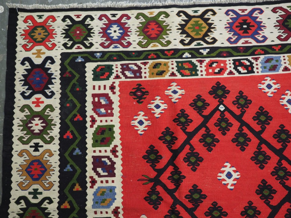 An antique red Pirot Sarkoy wool kilim rug featuring black and white geometric diamond motifs and multi-coloured decorative borders. View VI