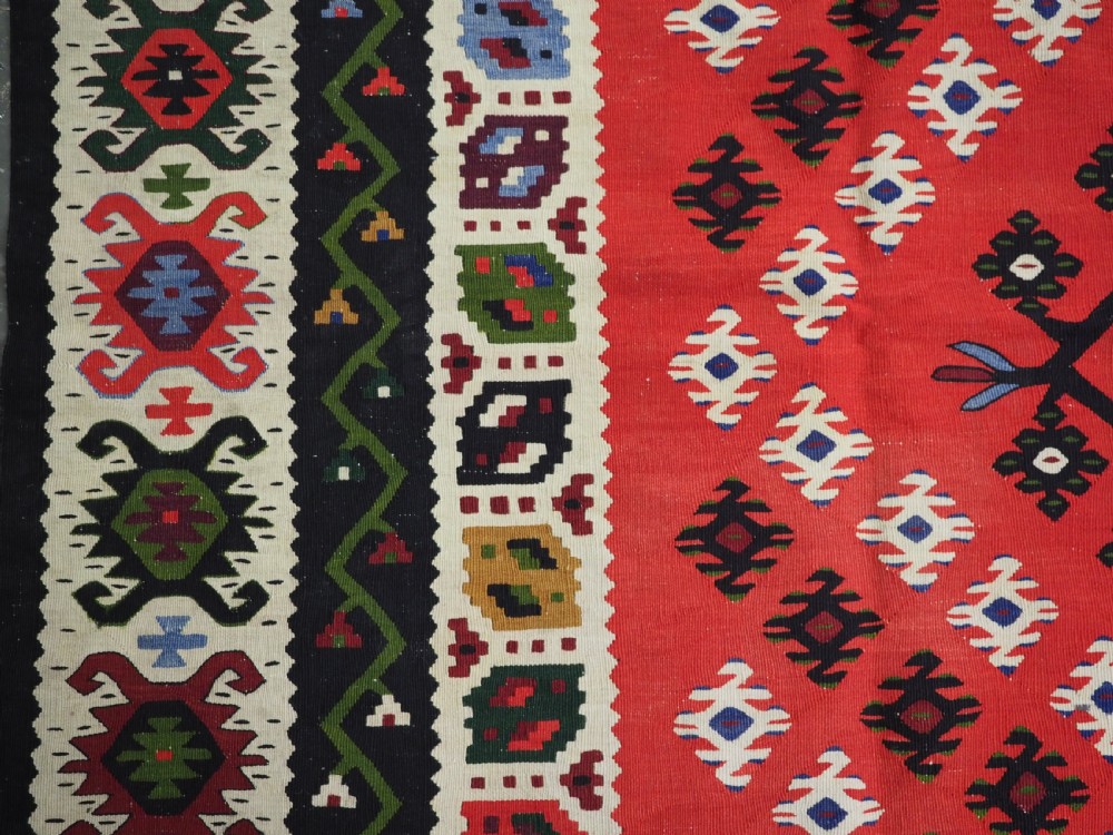 An antique red Pirot Sarkoy wool kilim rug featuring black and white geometric diamond motifs and multi-coloured decorative borders. View VII