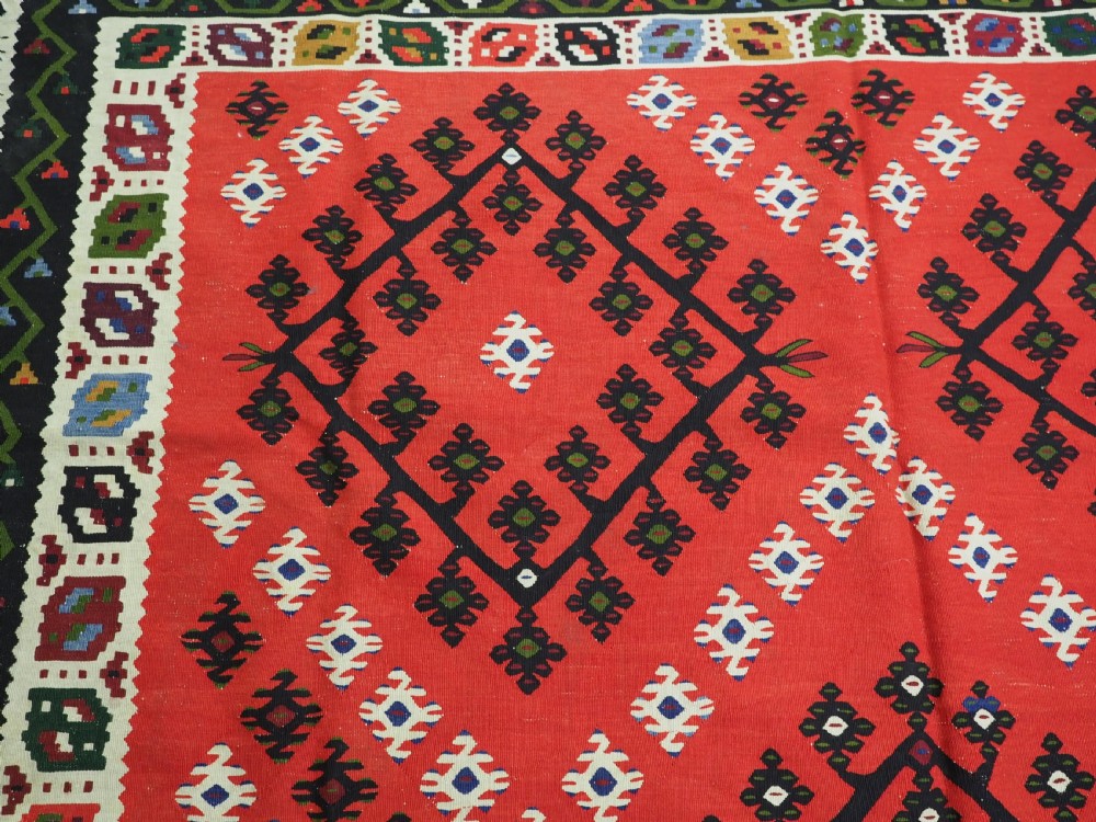 An antique red Pirot Sarkoy wool kilim rug featuring black and white geometric diamond motifs and multi-coloured decorative borders. View VIII