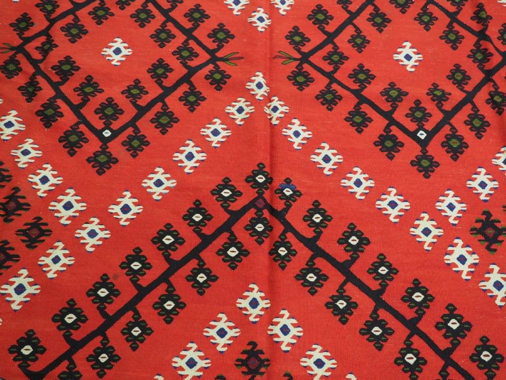 An antique red Pirot Sarkoy wool kilim rug featuring black and white geometric diamond motifs and multi-coloured decorative borders. View IX
