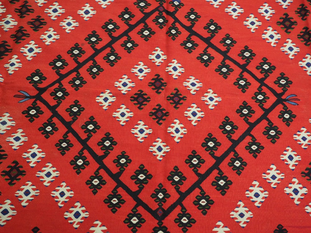 An antique red Pirot Sarkoy wool kilim rug featuring black and white geometric diamond motifs and multi-coloured decorative borders. View X