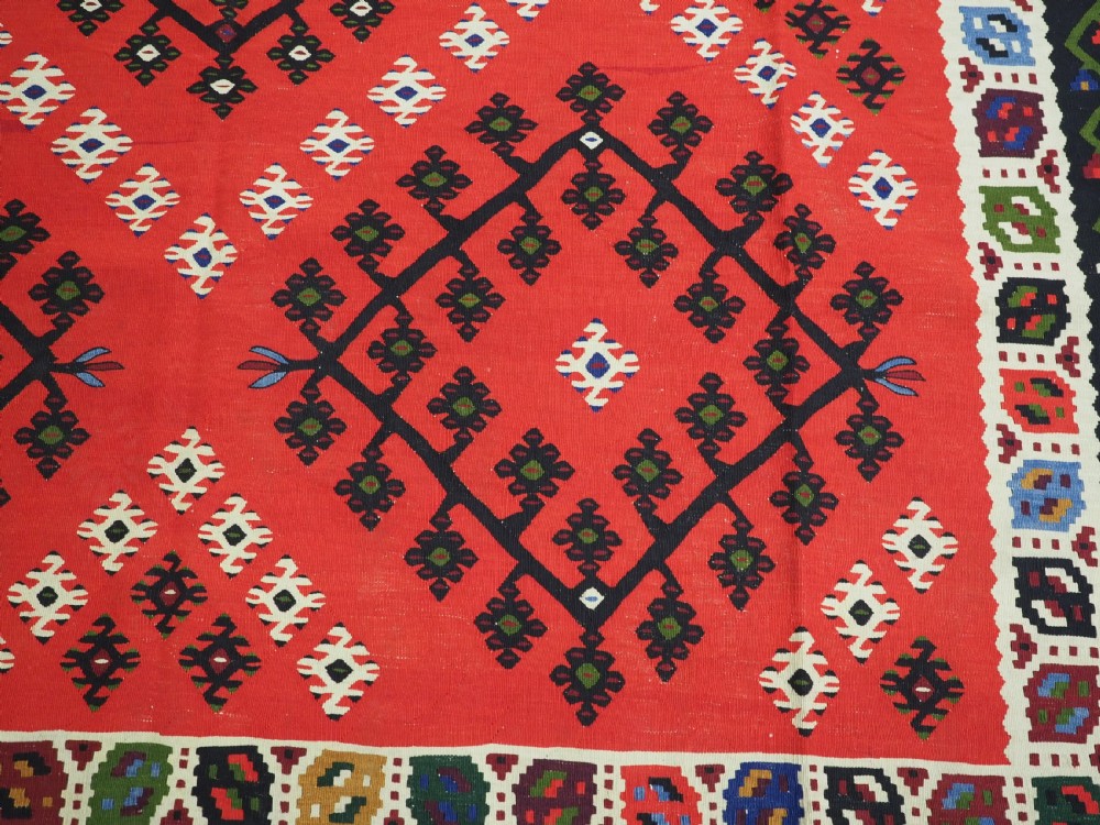An antique red Pirot Sarkoy wool kilim rug featuring black and white geometric diamond motifs and multi-coloured decorative borders. View XI