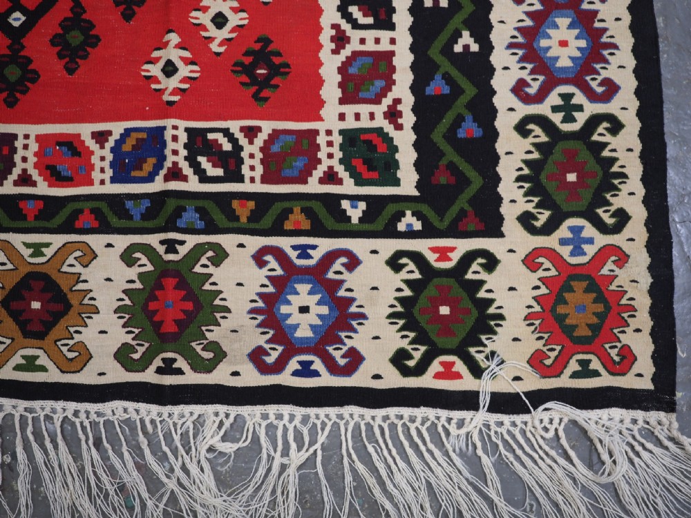 An antique red Pirot Sarkoy wool kilim rug featuring black and white geometric diamond motifs and multi-coloured decorative borders. View XII