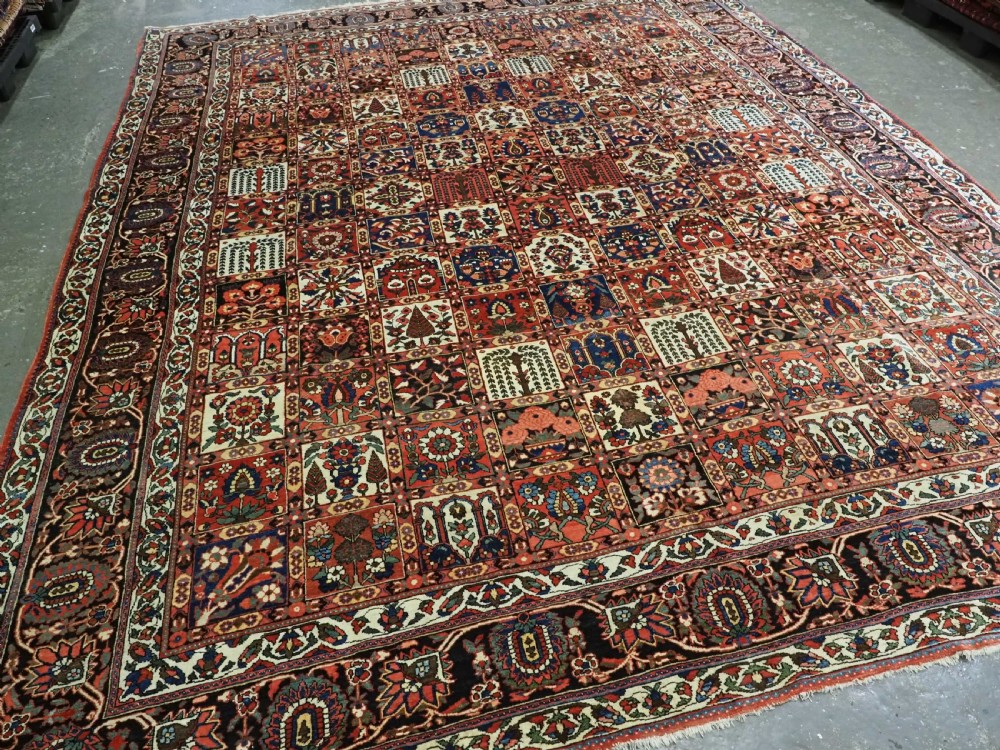 A large antique Bakhtiari wool carpet featuring a repeating grid pattern of garden motifs in terracotta red, navy blue, and ivory framed by a wide ornamental border. View II