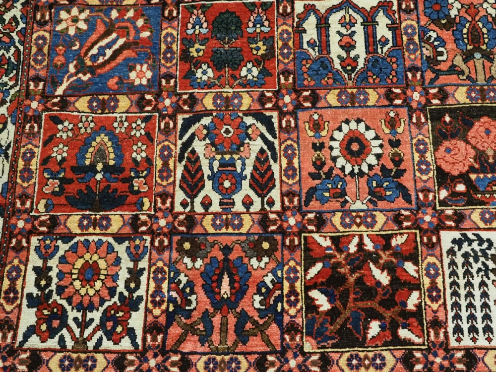 A large antique Bakhtiari wool carpet featuring a repeating grid pattern of garden motifs in terracotta red, navy blue, and ivory framed by a wide ornamental border. View VIII